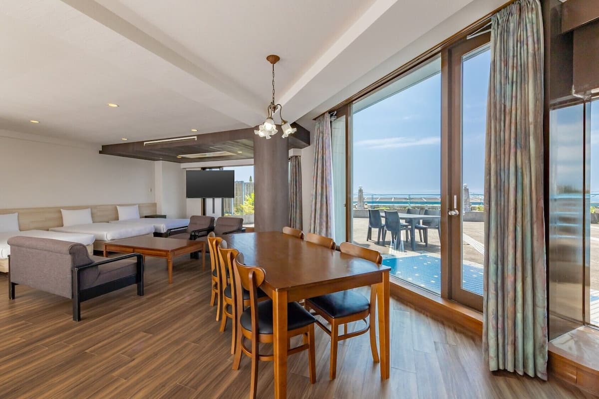 A modern hotel room with a dining area, sofa, and large windows offering a view.