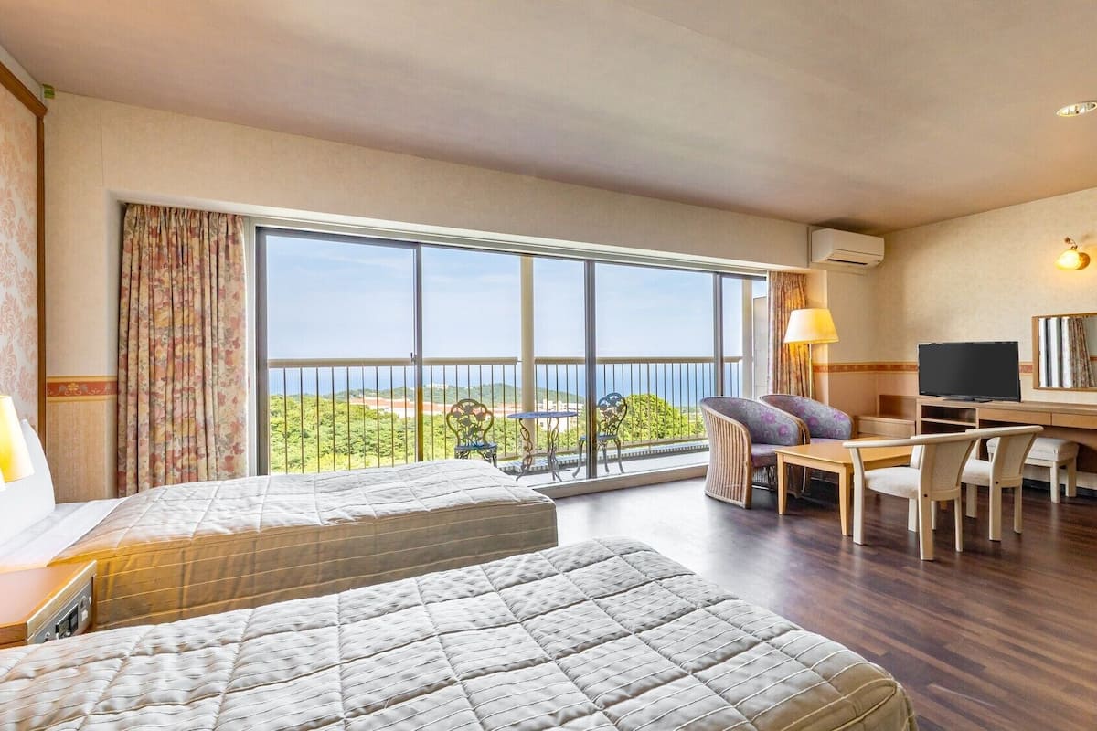 A hotel room with a balcony, a desk with a chair, a bed, and a TV.