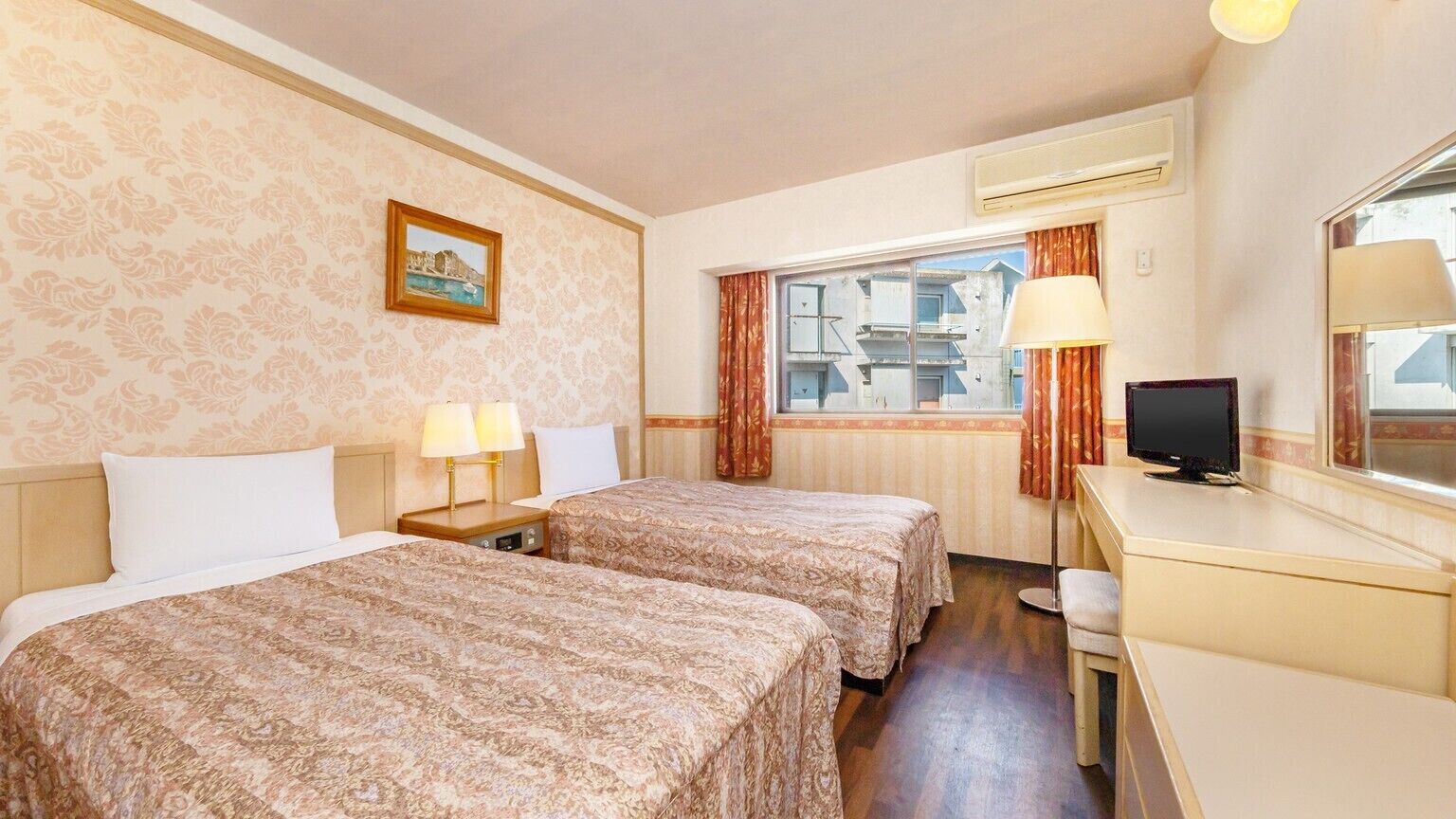 A hotel room with two beds, a desk, a television, and a window with curtains.