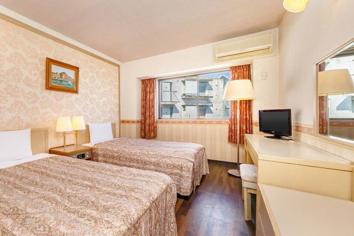 A hotel room with two beds, a desk, a television, and a window with curtains.