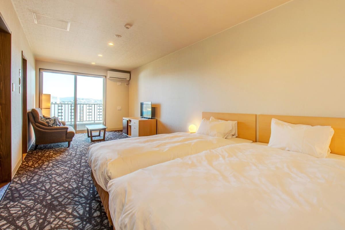 Une chambre d’hôtel avec deux lits, un bureau, une chaise et un balcon.