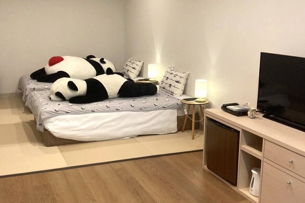 Une chambre à coucher comprenant un lit, des oreillers, une télévision, une table de chevet, une lampe, un haut-parleur et une armoire.