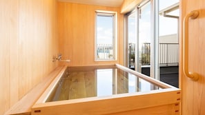 Una habitación de madera con una bañera de hidromasaje con vidrio, una puerta corrediza de vidrio a un balcón y una puerta de madera con manija.