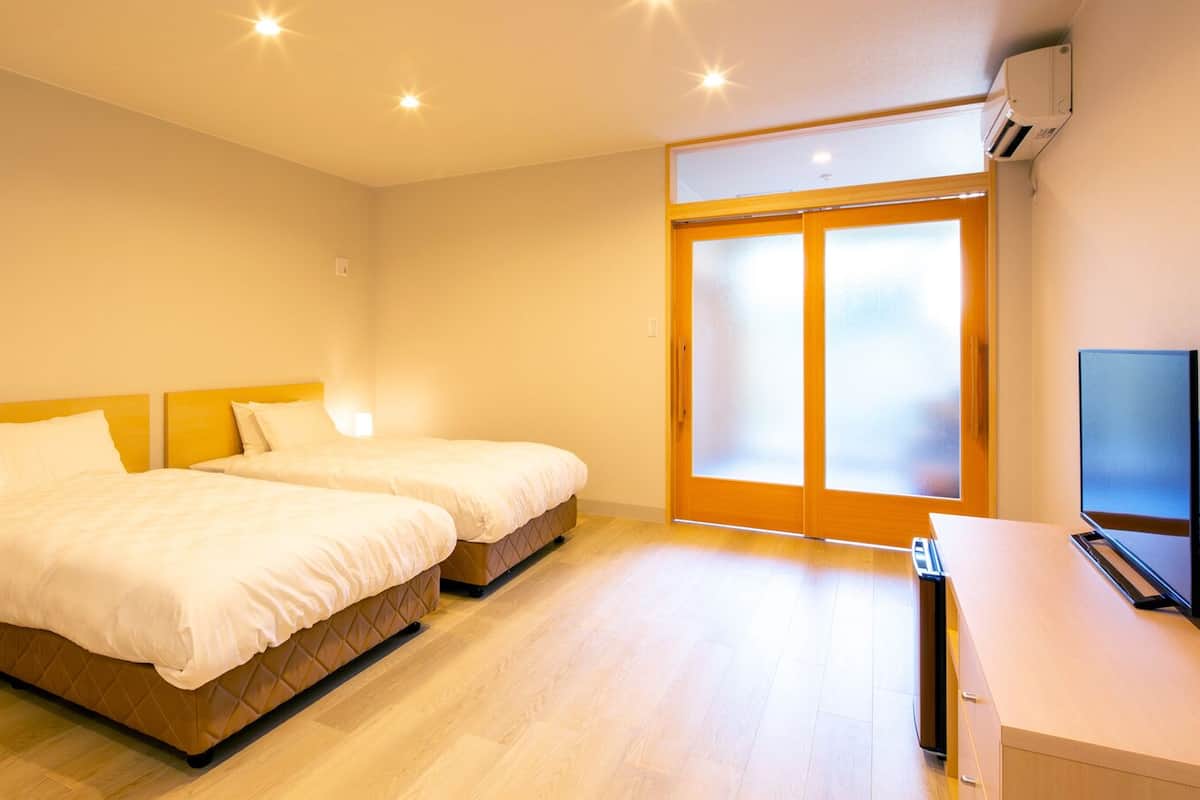 Une chambre d’hôtel avec deux lits, une télévision et une porte-fenêtre coulissante donnant sur l’extérieur.