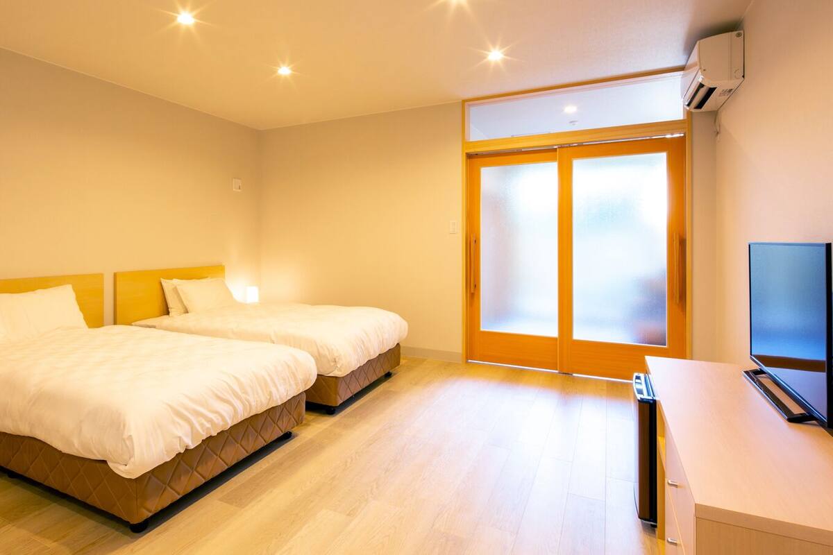 Ein Hotelzimmer mit zwei Betten, einem Fernseher und einer Schiebeglastür nach draußen.