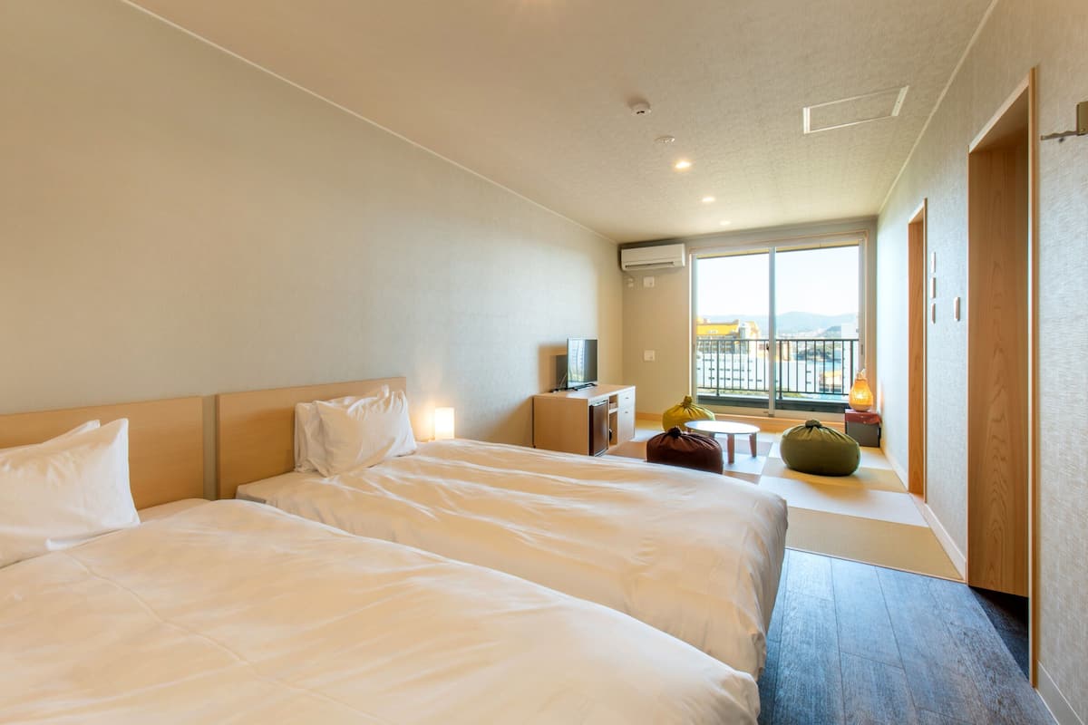 Une chambre d’hôtel avec deux lits, un bureau, une chaise, une petite table et une vue sur l’extérieur.