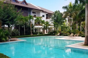 A swimming pool with lounge chairs, surrounded by palm trees and a multi-story building with balconies. - ®{Terrenas~Beach~Spot} Monserrat +Pool+5min Beach (Las Terrenas)