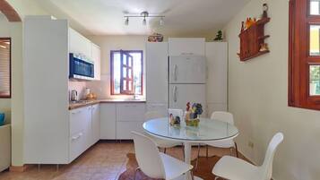 Una cocina compacta con armarios blancos, una mesa redonda de cristal y sillas blancas.