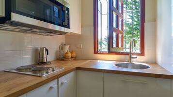 Una cocina con microondas, estufa, lavabo y ventana con vista a follaje.