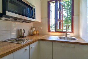 A kitchen with a microwave, stove, sink, and window with a view of greenery. - ®{Villa~Roseca~EcoLodge}@LosMogotes +Pool+Family (Dominican Republic)