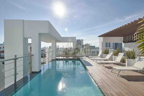 A rooftop swimming pool with a city view, surrounded by lounge chairs and potted plants. - ® LUX {Arpel} Experience @DowntownSD +Pool+Gym (Santo Domingo)