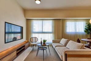 Ein modernes Wohnzimmer mit flachbildfernseher an der Wand, einem Sofa, einem Couchtisch und einem Sessel.