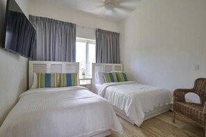 A hotel room with two beds, a flat-screen TV mounted on the wall, and a wicker chair. - ®{The~Palms~View}@PlayaBonita +Beachfront+Pool+BBQ (Las Terrenas)