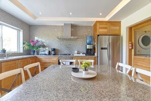 Eine moderne Küche mit Granit-Arbeitsplatten, Holzschränken, einem Edelstahl-Kühlschrank und einer integrierten Waschmaschine.