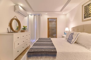 A bedroom with a bed, a dresser, a mirror, a painting, and a door leading to a bathroom. - ®{Monserrat Beach Condo} @Terrenas +Pool+Wifi+BBQ (Las Terrenas)