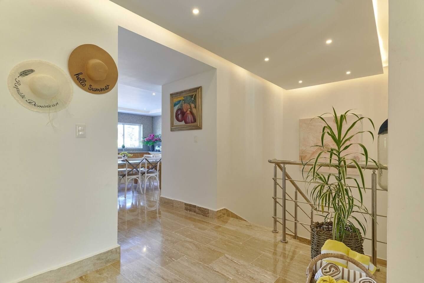 A hallway with a staircase, a dining area in the background, and a plant on the right.