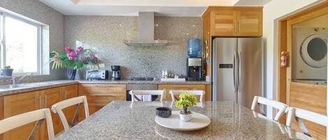 A modern kitchen with granite countertops, wooden cabinets, a stainless steel refrigerator, and a built-in washing machine.