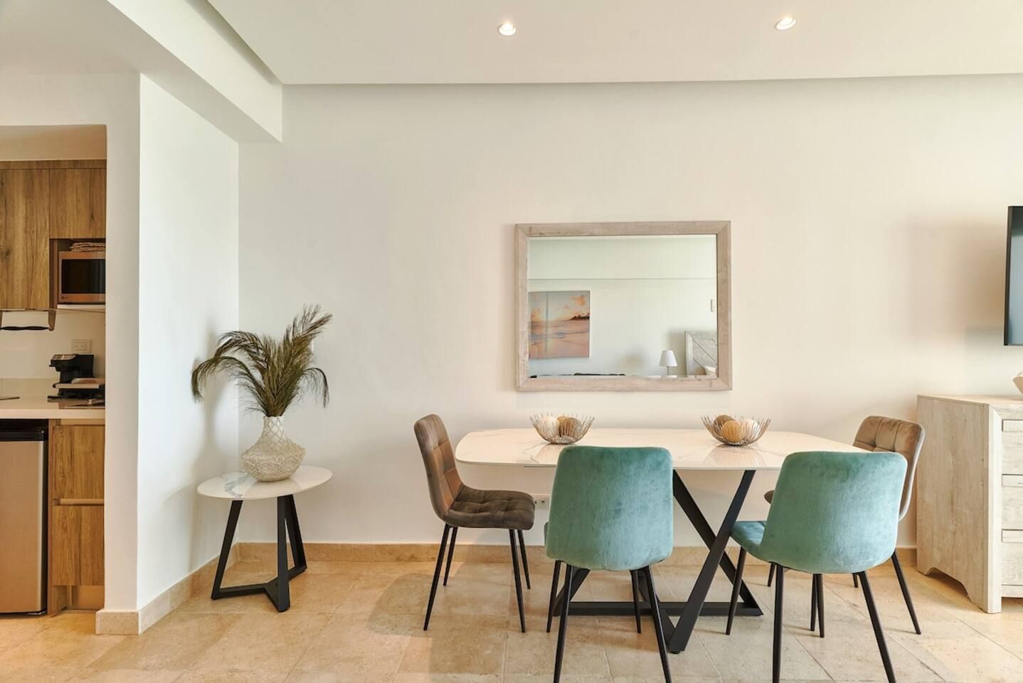 A modern dining area with a white table, teal chairs, and a decorative plant.
