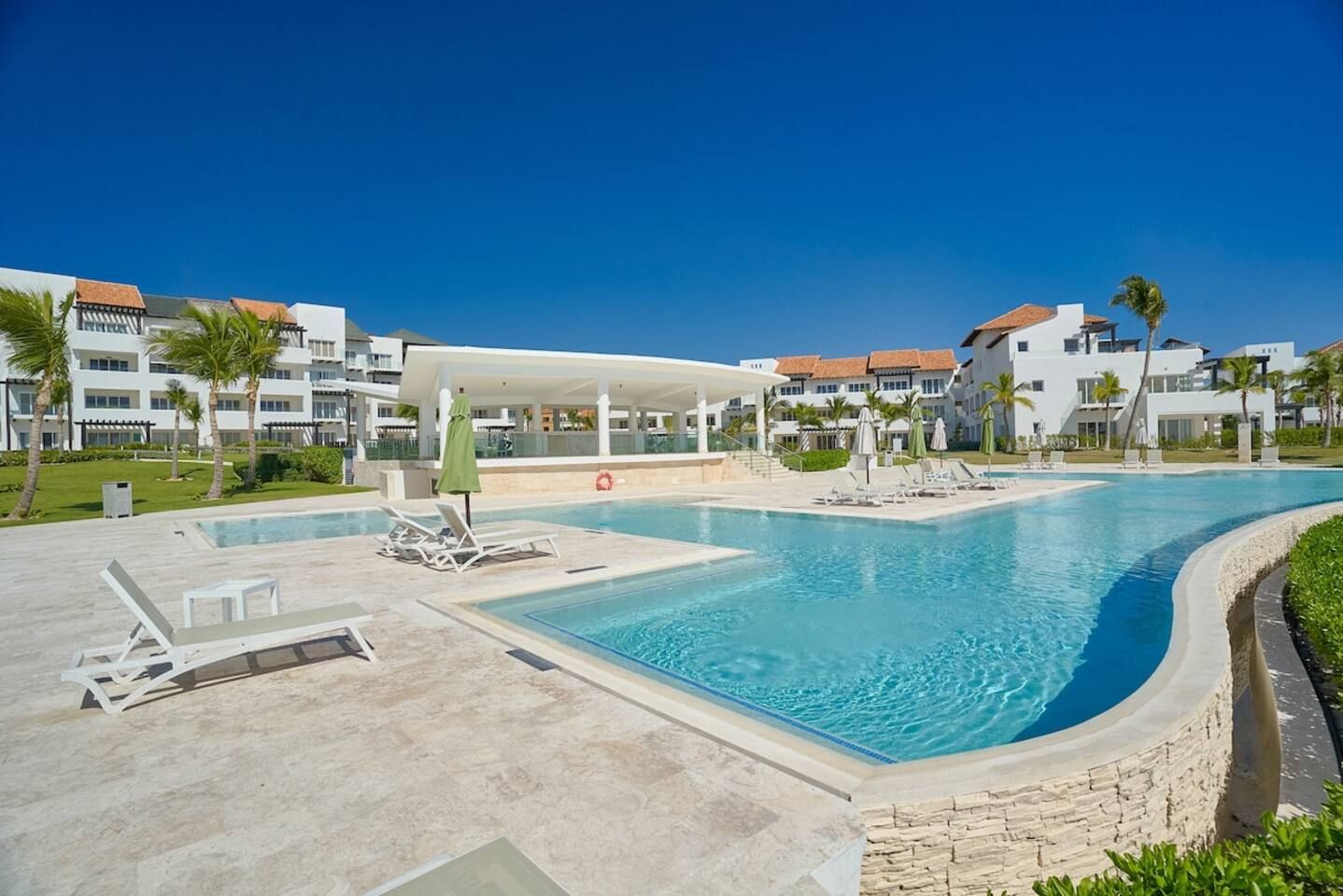 A swimming pool area with lounge chairs, a covered seating area, and a view of hotel buildings.