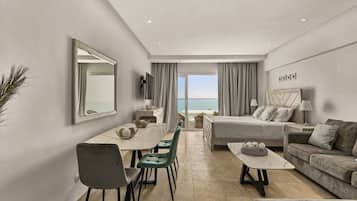 A modern hotel room with a bed, a sofa, a dining table, and a TV.