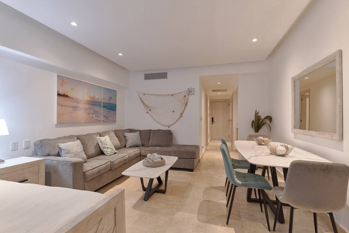A modern living room with a sectional sofa, a dining table with chairs, a coffee table, and a large painting on the wall.