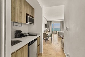 A modern kitchen with a built-in microwave, a coffee machine, and a dishwasher. There is a dining area with a table and chairs, and a view of the sea through large windows. - ®The{Beach~Spot} @CapcanaParadise +Pool+Beachfront (Punta Cana)