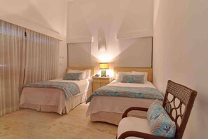 Une chambre d’hôtel avec deux lits, une table de chevet, une lampe et un fauteuil en osier.