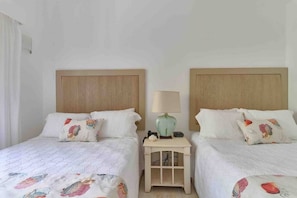 Ein Hotelzimmer mit zwei Betten, jeweils mit Kopfteil, Nachttisch und Lampe, sowie dekorativen Kissen.