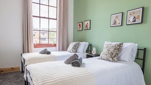 A twin room with two beds, a window with curtains, and artwork on the wall.