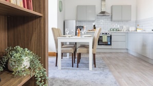 A modern kitchen with white cabinets, a dining table with chairs, and a bookshelf with books.