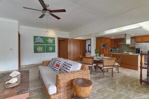 A spacious living area with a sofa, dining table, and chairs, a kitchen with wooden cabinets, and a ceiling fan. - ®{The~beach~condo} @Balcones del Atlantico (El Limón)