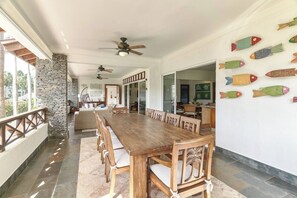A spacious dining area with a long wooden table and chairs, a stone wall, and a ceiling fan. - ®{The~beach~condo} @Balcones del Atlantico (El Limón)
