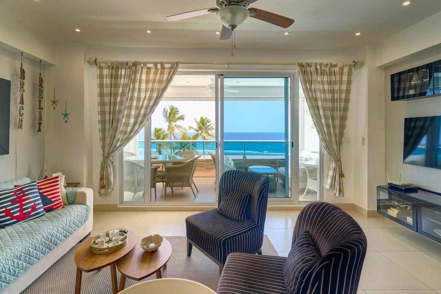 Une chambre d’hôtel avec un balcon, un canapé, un fauteuil à rayures, une table basse et un téléviseur.