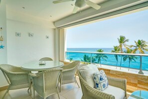 A balcony with a view of the ocean and palm trees, wicker furniture, and a ceiling fan. - ®{Las~Olas~Beach~Condo}@JuanDolio +BeachFront+Pool (Juan Dolio)
