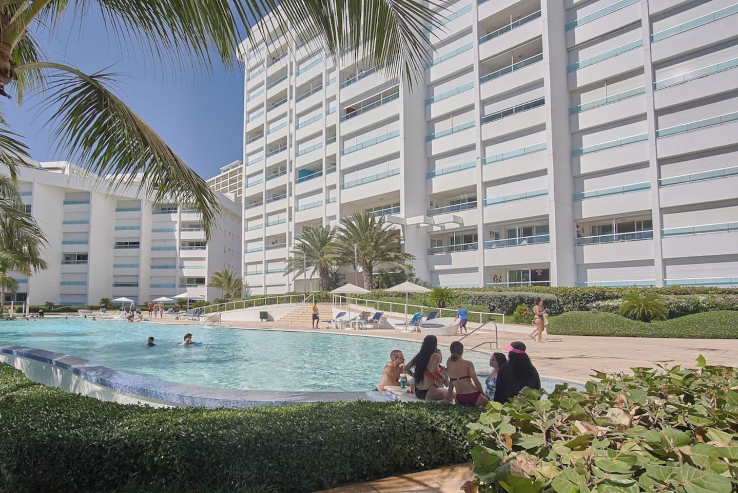 Un hotel con piscina rodeada de palmeras y sillones de descanso.
