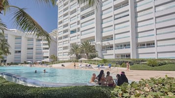 Un hotel con piscina rodeada de palmeras y sillones de descanso.