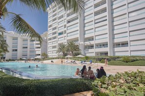 Un hotel con piscina rodeada de palmeras y sillones de descanso.