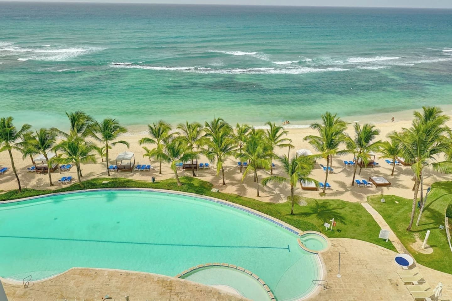 A resort with a swimming pool, beach, and palm trees.