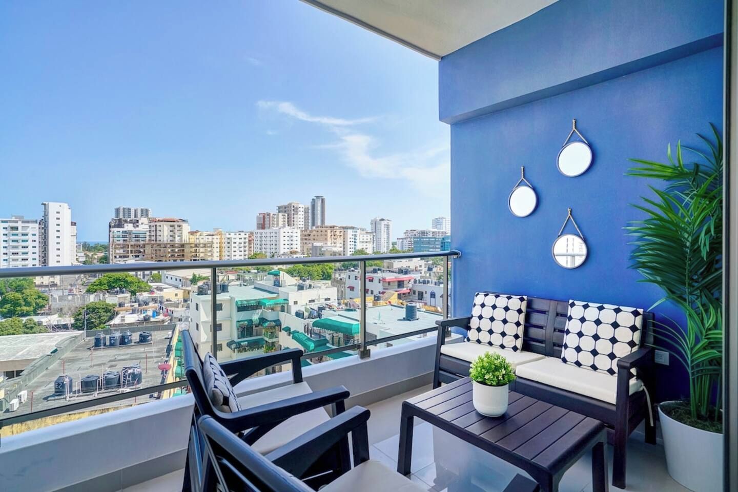 A balcony with a city view, a sofa, two chairs, a table, and a potted plant.