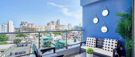 A balcony with a city view, a sofa, two chairs, a table, and a potted plant.