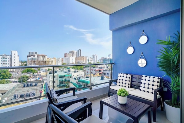 A balcony with a city view, a sofa, two chairs, a table, and a potted plant. - ® 2BR{Ajega~Views} @Downtown SDQ +Pool+Gym (Santo Domingo)