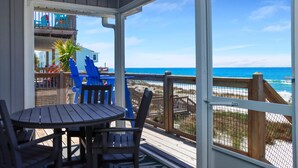 A covered outdoor area with a table and chairs, a view of the beach, and a wooden deck. - My Tide (Port St. Joe)