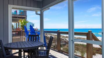 Un espacio al aire libre cubierto con una mesa y sillas, vista a la playa y una terraza de madera.