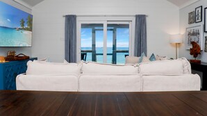 A living room with a white sofa, a wooden floor, a large window with a view of the sea, and a mounted fish on the wall. - My Tide (Port St. Joe)