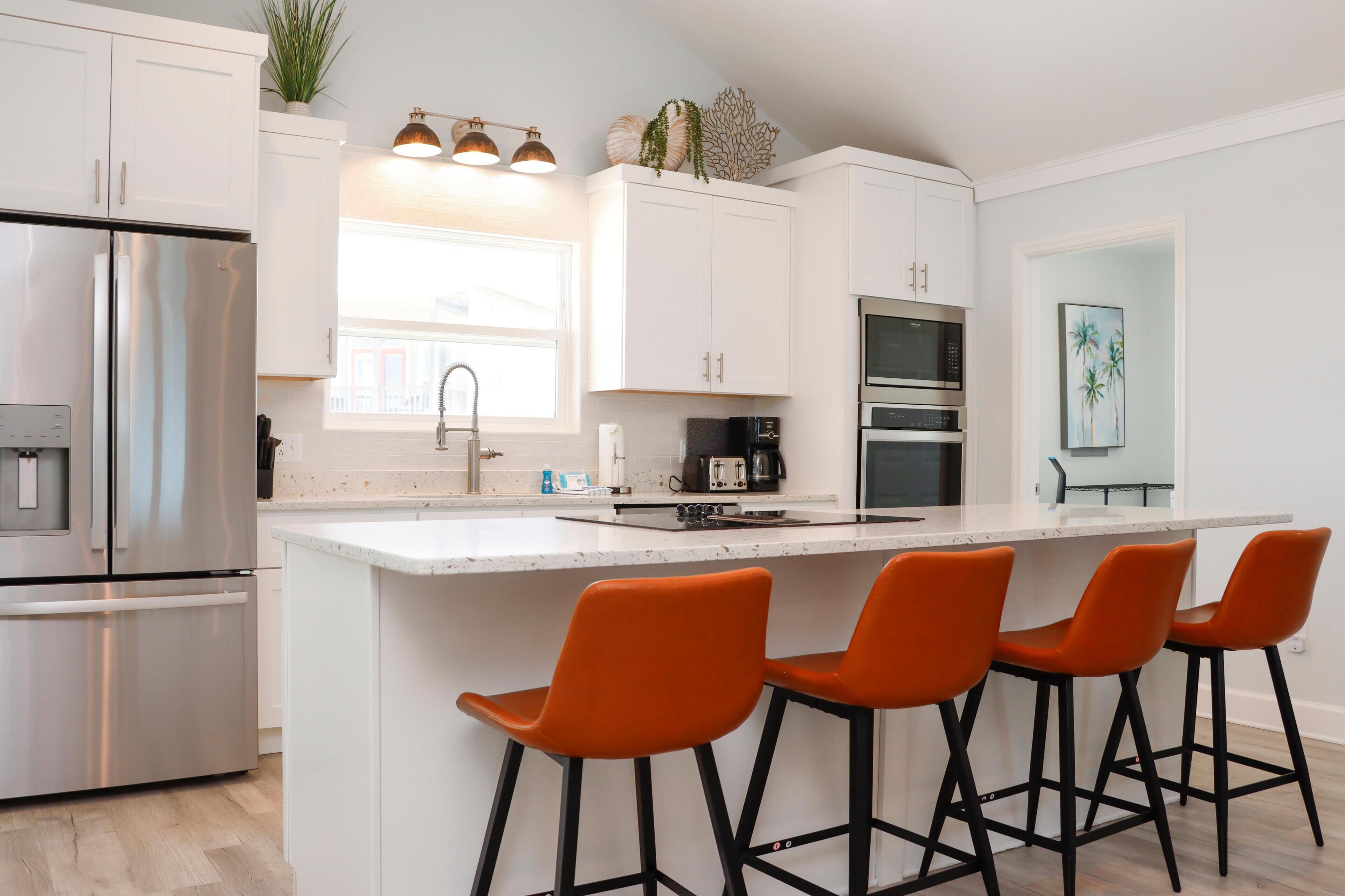 A modern kitchen with white cabinets, stainless steel appliances, and orange bar stools.