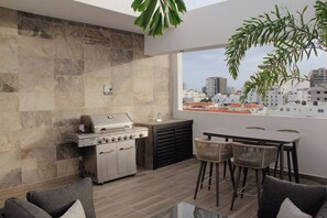 An outdoor kitchen with a grill, dining table, and chairs, overlooking a cityscape. - ®2BR{Santorini~Views} @Downtown SDQ +Lounge+Gym (Santo Domingo)