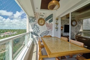 Ein Balkon mit Esstisch und Stühlen, einer Wanduhr und einem Fernseher.