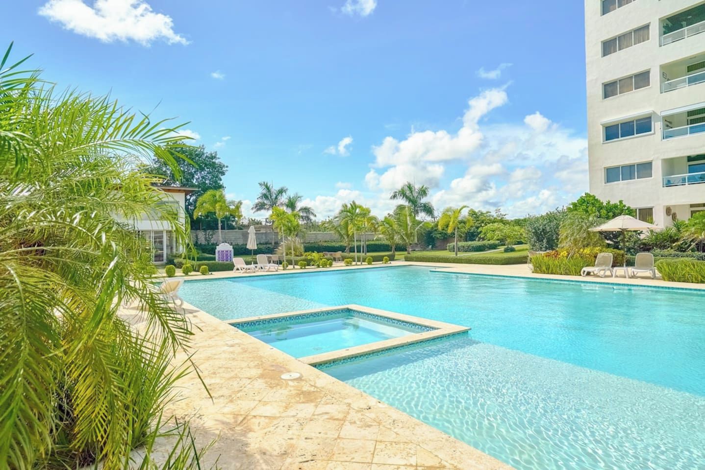Ein Swimmingpool mit klarem, blauem Wasser, umgeben von Palmen und Liegestühlen.