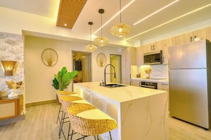 A modern kitchen with a marble island, stainless steel appliances, and wicker bar stools. - ®{3BR~Coral Cliffs~Views} @JuanDolio + Pool + Gym (Juan Dolio)