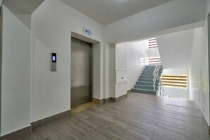 Un interno moderno con pavimento in legno, una scala con corrimano e un pannello di controllo dell'ascensore a parete.